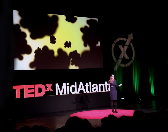 hasini on stage with behind her an abstract image of cancer spreading